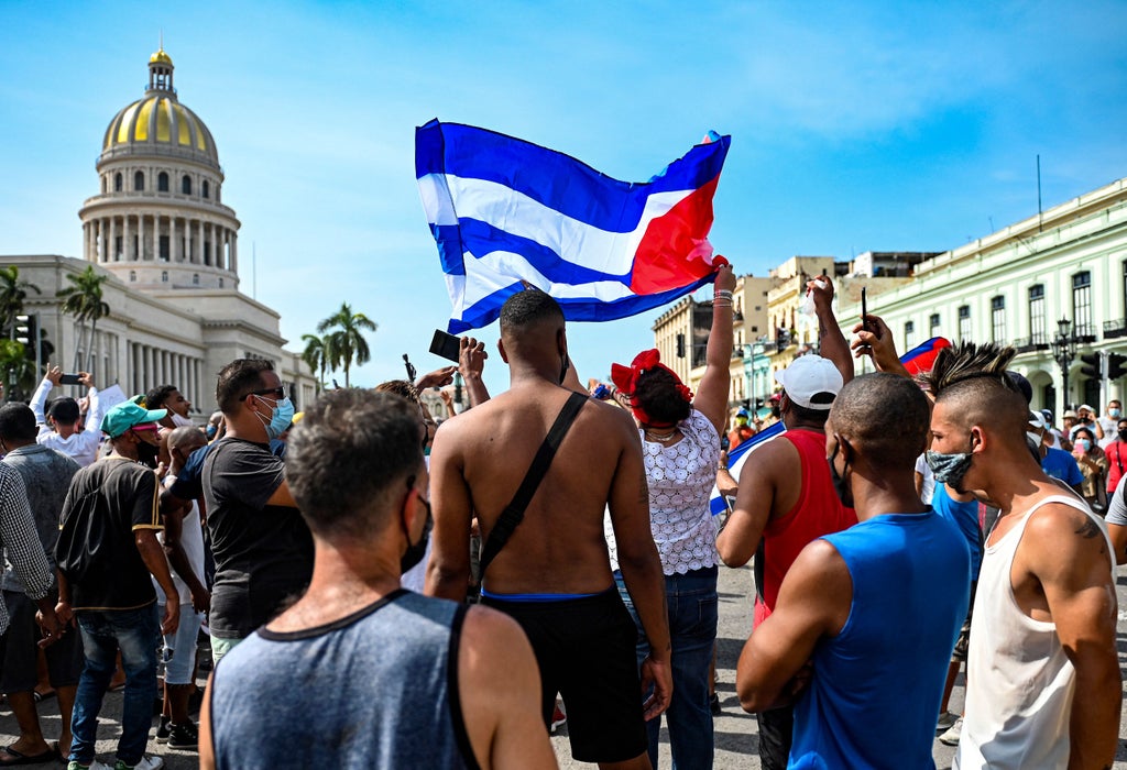 一群人站在人群前：古巴人呼吁米格尔·迪亚兹-卡内尔总统辞职 - 法新社通过盖蒂图片社